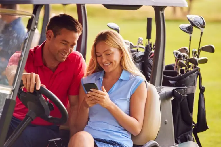 Couple Sitting In Golf Buggy On Course With Woman Using Mobile Phone